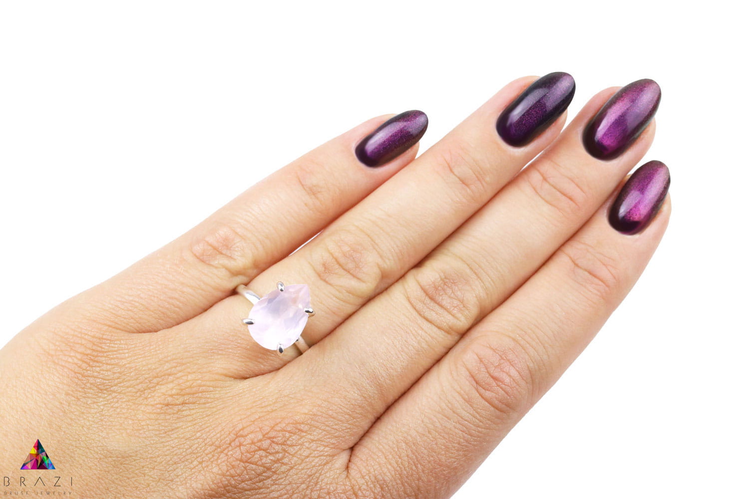 Pierścionek z naturalnym kwarcem różowym w srebrnej oprawie na dłoni z ciemnym manicure, biżuteria Brazi.