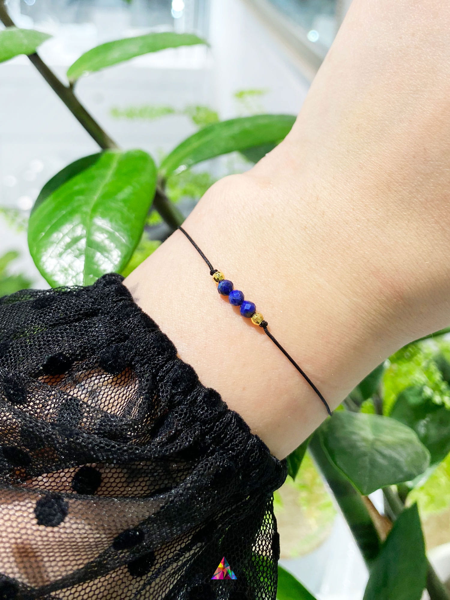 Bransoletka z naturalnym lapis lazuli na nadgarstku modelki, czarny sznurek i złote detale, marka Brazi.