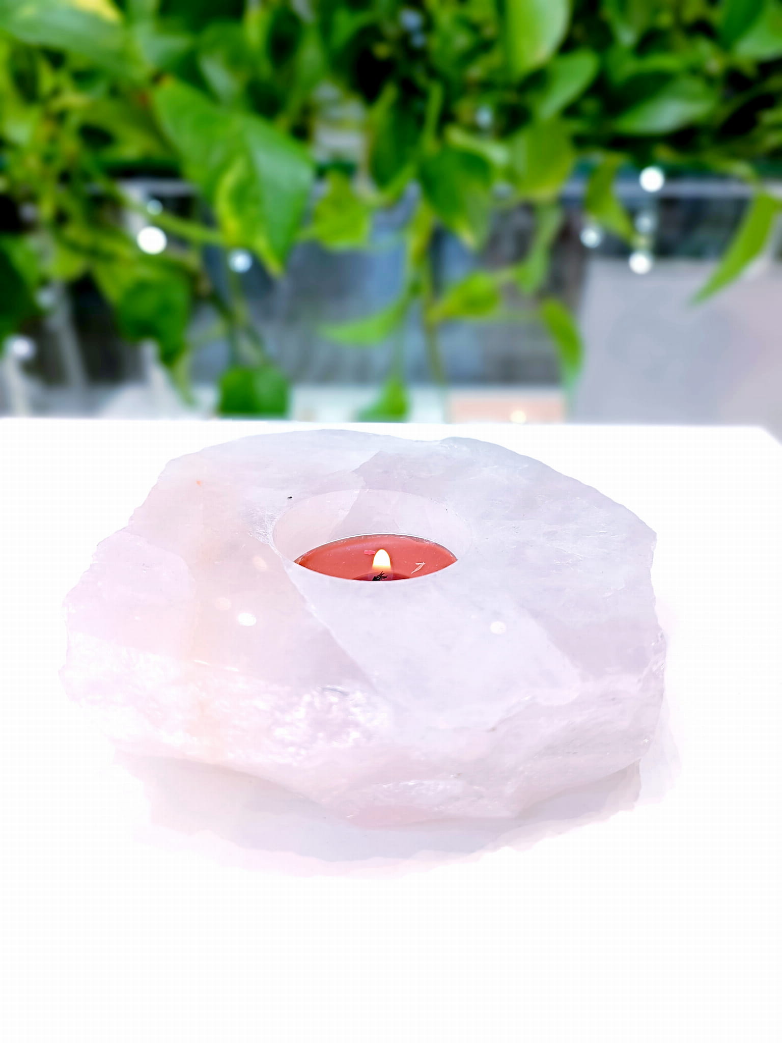 Świecznik z naturalnego kwarcu różowego z zapaloną świecą typu tealight na jasnym blacie, biżuteria Brazi.