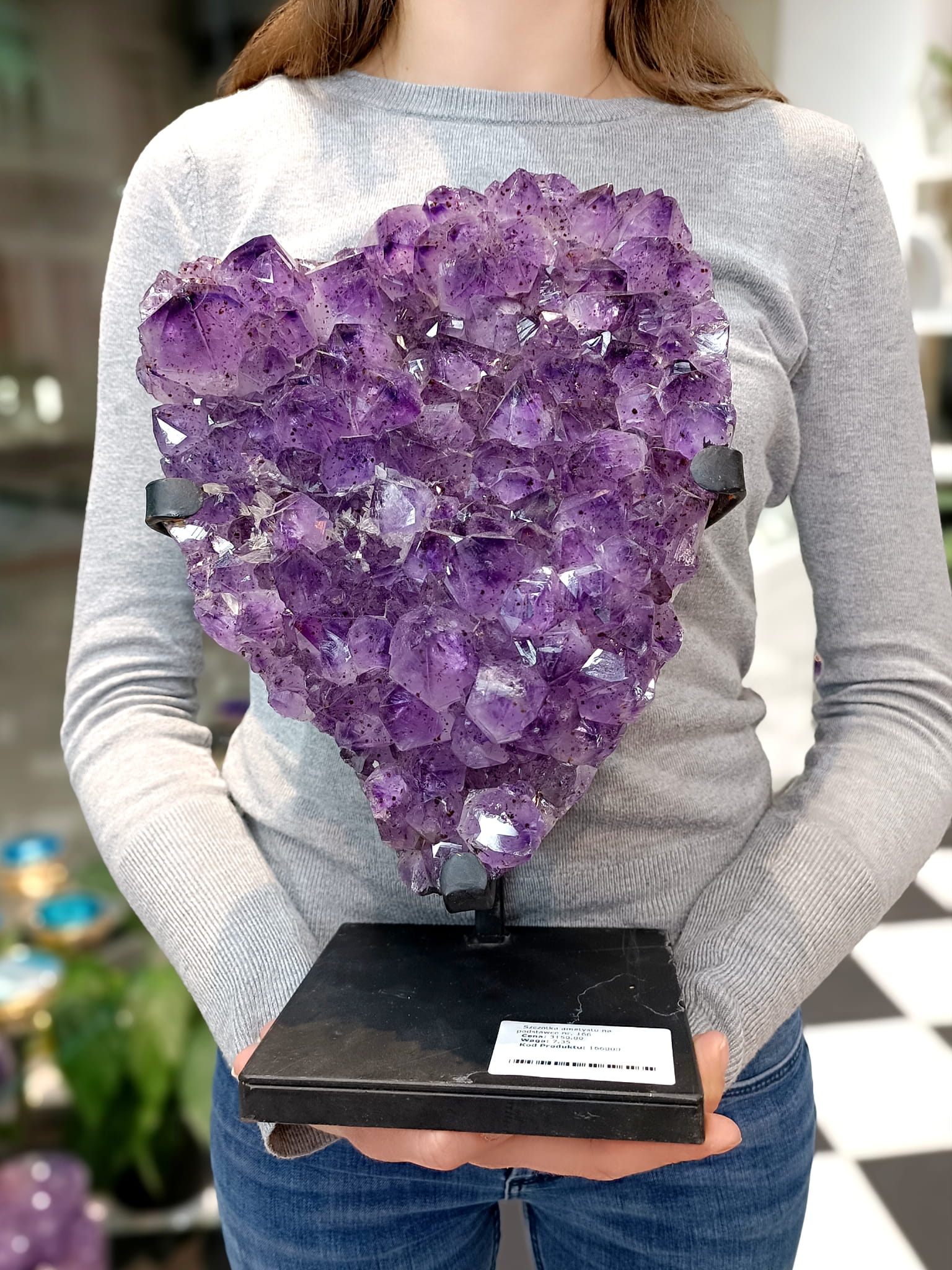Naturalny ametyst na stojaku trzymany w dłoni, prezentacja skali i wielkości bryły nr 166, Brazi Druse Jewelry.