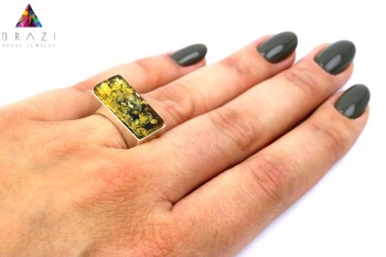 Pierścionek z zielonym bursztynem i srebrem prezentowany na palcu dłoni, biżuteria Brazi