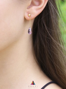 Złoty kolczyk z naturalnym ametystem w kształcie kropli prezentowany na uchu modelki, marka Brazi