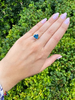 Złoty pierścionek z topazem London Blue o szlifie trylion na dłoni modelki, biżuteria Brazi.