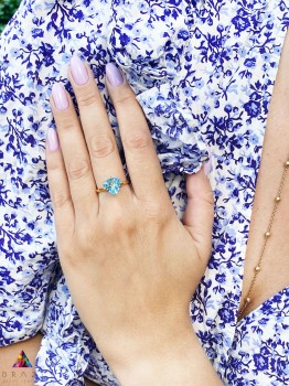 Złoty pierścionek z błękitnym topazem sky blue o szlifie trylion na dłoni, marka Brazi.