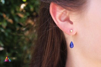 Złote kolczyki z wiszącym lapis lazuli zaprezentowane na uchu modelki, biżuteria Brazi