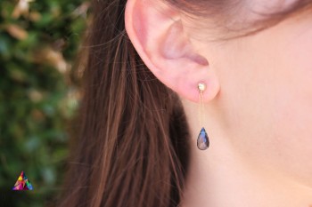 Złote kolczyki z naturalnym topazem London Blue w kształcie kropli na uchu modelki, marka Brazi