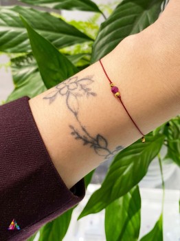 Bransoletka z czerwonego sznurka z naturalnym rubinem prezentowana na kobiecym nadgarstku, biżuteria Brazi.