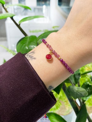 Bransoletka z fasetowanym rubinem i turmalinem na nadgarstku, złote detale i beżowy sznurek, biżuteria Brazi