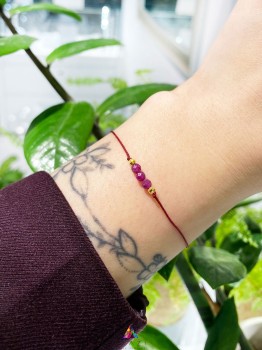 Bransoletka z fasetowanym rubinem na czerwonym sznurku na nadgarstku modelki, biżuteria Brazi