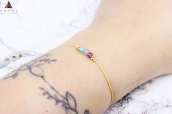 Bransoletka z minerałów na nadgarstku z tatuażem na tle jasnego marmuru, marka Brazi