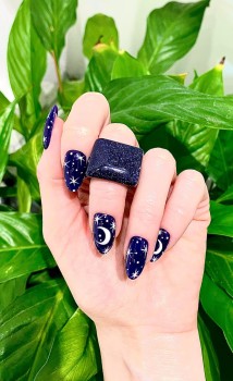 Pierścionek Noc Kairu prezentowany na dłoni modelki z kosmicznym manicure na tle zielonych roślin.