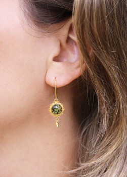 Złoty kolczyk z zielonym bursztynem prezentowany na uchu modelki, biżuteria marki Brazi