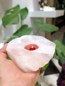 Świecznik z kwarcu różowego z płonącą świeczką trzymany w dłoni, pokazujący wielkość produktu marki Brazi.