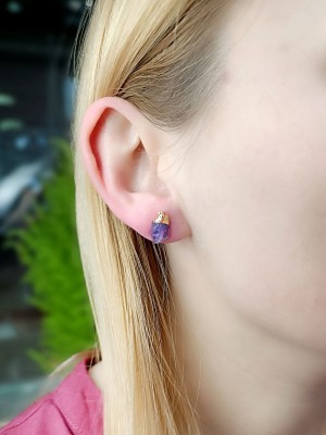 Złocone kolczyki z naturalnym ametystem w formie surowej bryłki na uchu modelki, biżuteria Brazi.