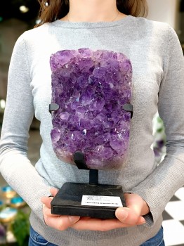 Szczotka naturalnego ametystu na metalowej podstawce trzymana w dłoniach, dekoracja marki Brazi