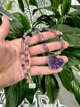 Pozłacany naszyjnik z ametystowym sercem i fluorytem trzymany w dłoni, detale kamieni naturalnych Brazi.