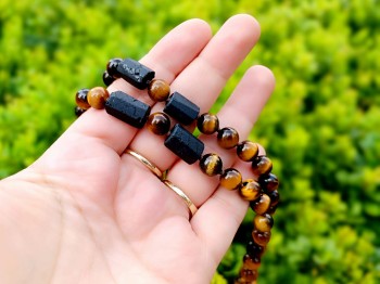 Naszyjnik z surowym turmalinem i tygrysim okiem trzymany w dłoni, naturalna biżuteria Brazi.