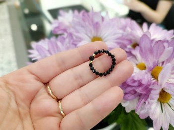 Elastyczny pierścionek z czarnego turmalinu trzymany w dłoni na tle kwiatów, marka Brazi