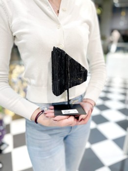 Czarny turmalin na podstawce trzymany w dłoniach, prezentacja skali naturalnego kamienia Brazi