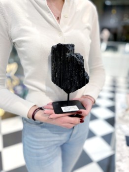 Czarny turmalin na podstawce trzymany w dłoniach, prezentacja skali naturalnego minerału Brazi