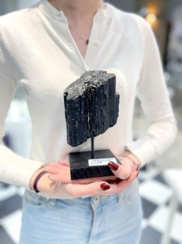 Czarny turmalin na podstawce trzymany w dłoniach, naturalny kamień dekoracyjny o surowej formie od Brazi.